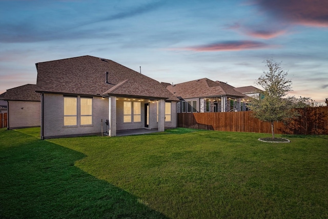 back house at dusk featuring a patio and a yard