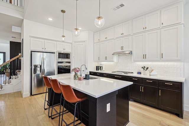 kitchen featuring stainless steel appliances, white cabinetry, sink, an island with sink, and light hardwood / wood-style floors