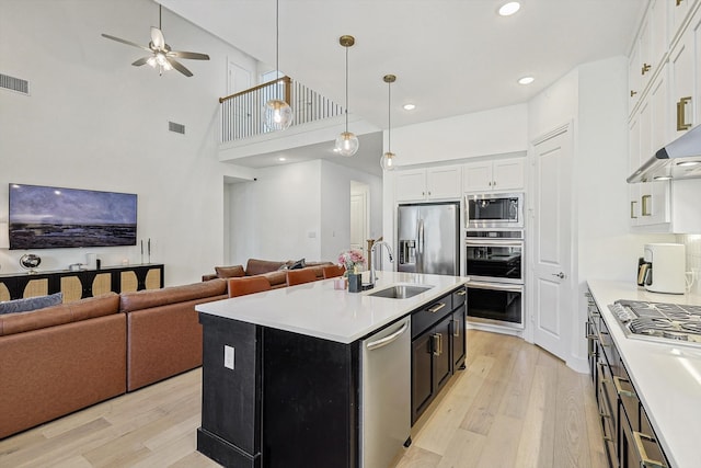 kitchen featuring stainless steel appliances, a center island with sink, sink, light hardwood / wood-style flooring, and a high ceiling