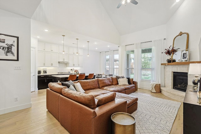 living room with high vaulted ceiling, light wood-type flooring, ceiling fan, and a brick fireplace