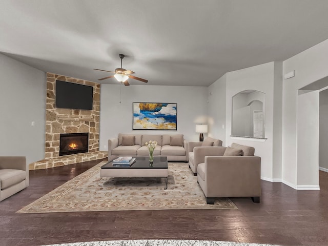 living room featuring ceiling fan, dark hardwood / wood-style flooring, and a stone fireplace