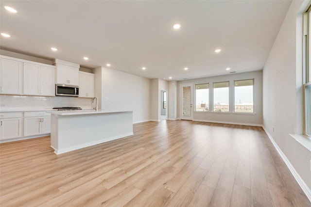 kitchen featuring white cabinetry, a kitchen island with sink, tasteful backsplash, and light hardwood / wood-style flooring