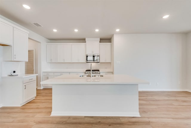 kitchen featuring sink, white cabinetry, tasteful backsplash, light hardwood / wood-style floors, and an island with sink