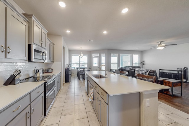 kitchen with sink, gray cabinets, appliances with stainless steel finishes, an island with sink, and decorative backsplash