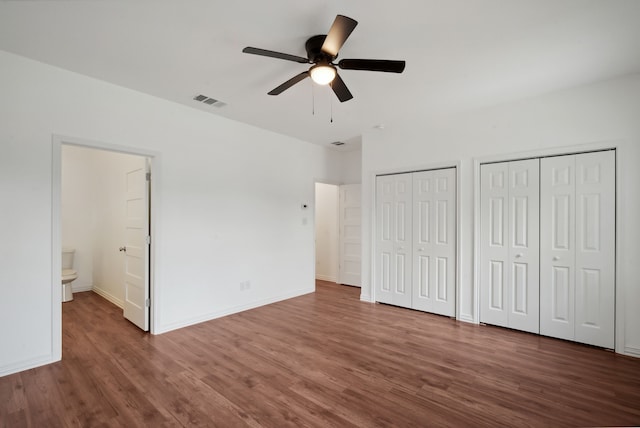 unfurnished bedroom featuring multiple closets, ensuite bathroom, dark hardwood / wood-style floors, and ceiling fan