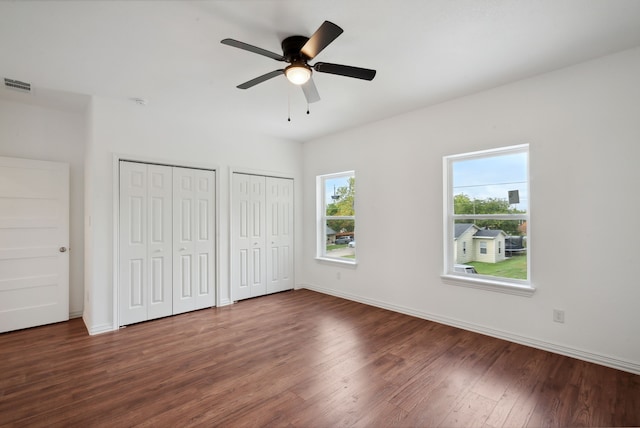 unfurnished bedroom with ceiling fan, multiple closets, and dark hardwood / wood-style floors