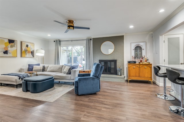 living room featuring hardwood / wood-style floors, ceiling fan, ornamental molding, and a fireplace