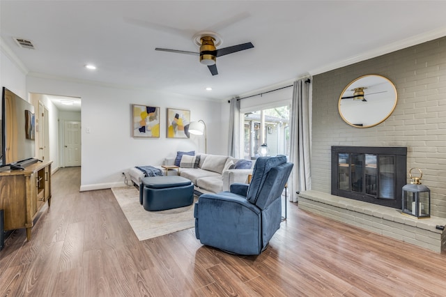 living room featuring hardwood / wood-style flooring, ceiling fan, crown molding, and a brick fireplace