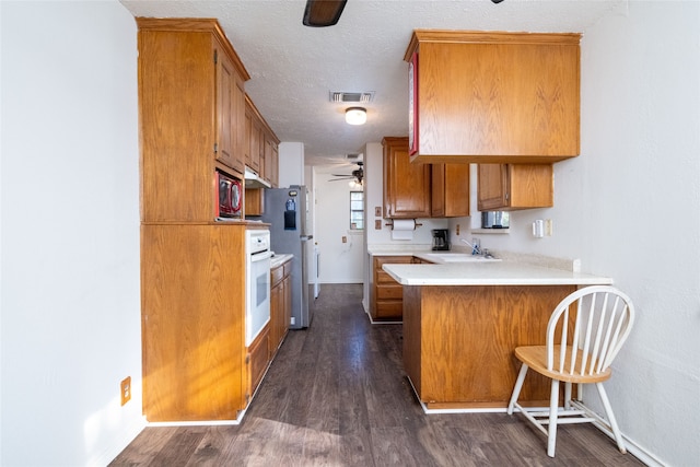 kitchen with appliances with stainless steel finishes, sink, a textured ceiling, kitchen peninsula, and dark wood-type flooring