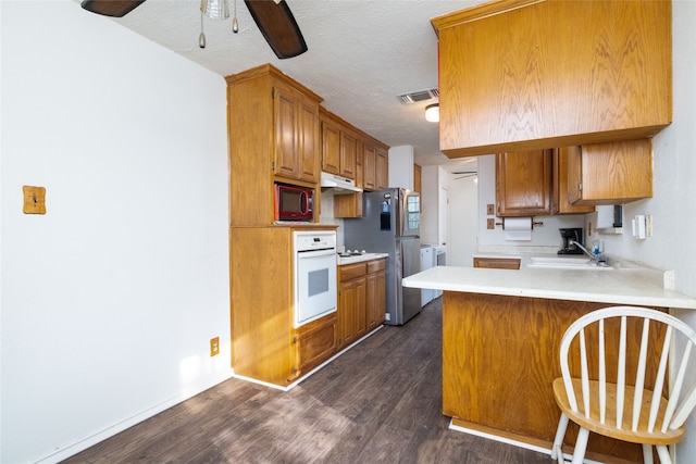 kitchen featuring oven, kitchen peninsula, stainless steel fridge, a textured ceiling, and dark hardwood / wood-style flooring