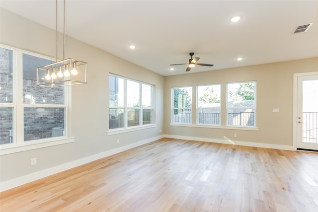 empty room with ceiling fan with notable chandelier and light wood-type flooring