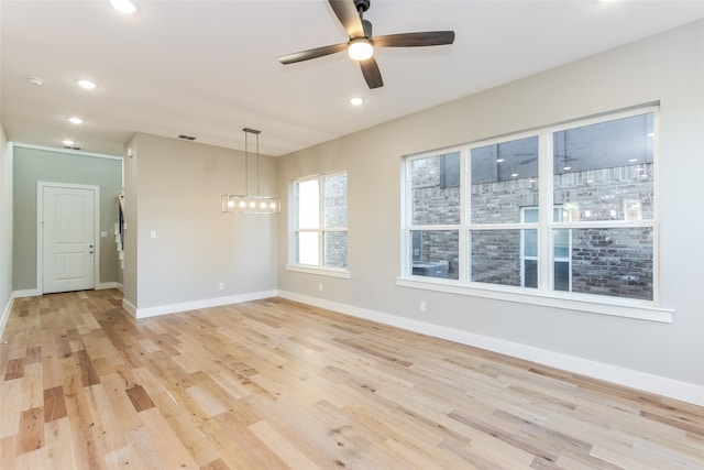 empty room with light wood-type flooring and ceiling fan with notable chandelier