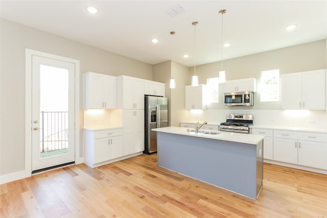 kitchen with hanging light fixtures, a center island with sink, light wood-type flooring, white cabinetry, and appliances with stainless steel finishes