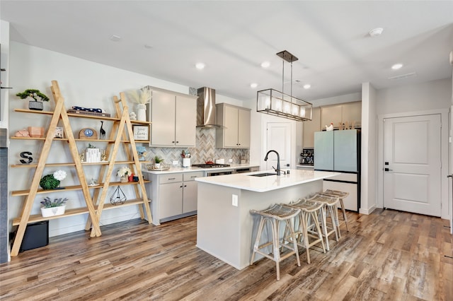 kitchen with wall chimney range hood, sink, pendant lighting, white fridge, and light hardwood / wood-style flooring