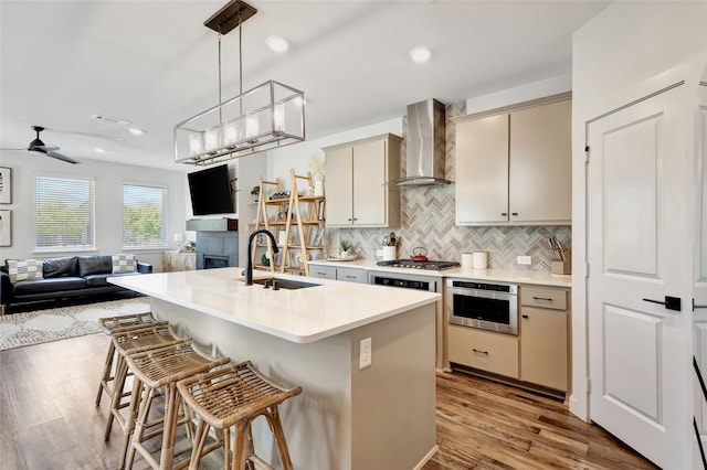 kitchen featuring wall chimney range hood, cream cabinets, stainless steel appliances, sink, and light hardwood / wood-style floors