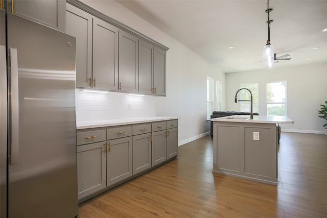 kitchen featuring gray cabinetry, light hardwood / wood-style floors, a center island with sink, and stainless steel fridge