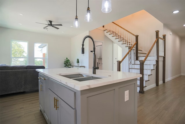 kitchen featuring a center island with sink, light stone countertops, dark hardwood / wood-style floors, pendant lighting, and sink