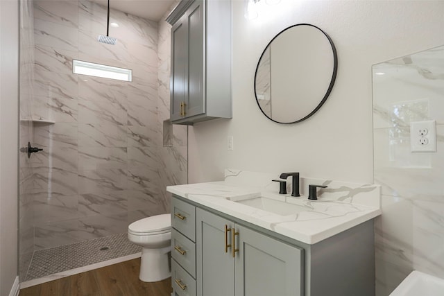 bathroom with toilet, hardwood / wood-style flooring, vanity, and tiled shower