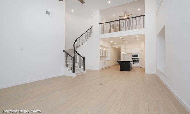 2414 Plumeria Ln, Celina, TX 75009 - unfurnished living room with light wood-style floors, ceiling fan, a towering ceiling, and visible vents