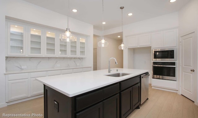 kitchen featuring tasteful backsplash, a center island with sink, light wood-type flooring, sink, and stainless steel appliances