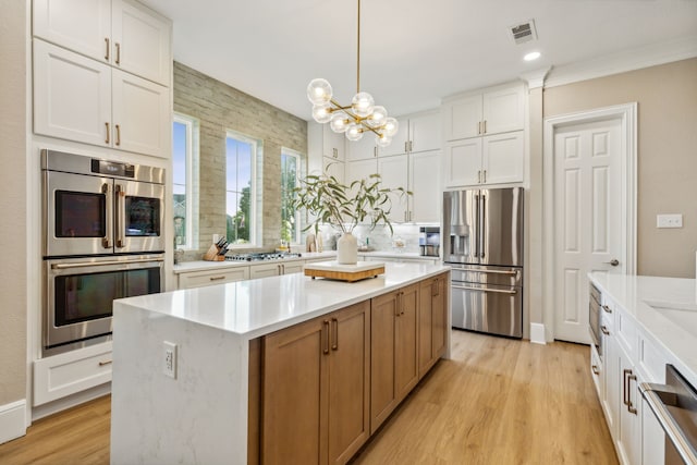 kitchen featuring a center island, stainless steel appliances, decorative light fixtures, white cabinets, and light hardwood / wood-style flooring