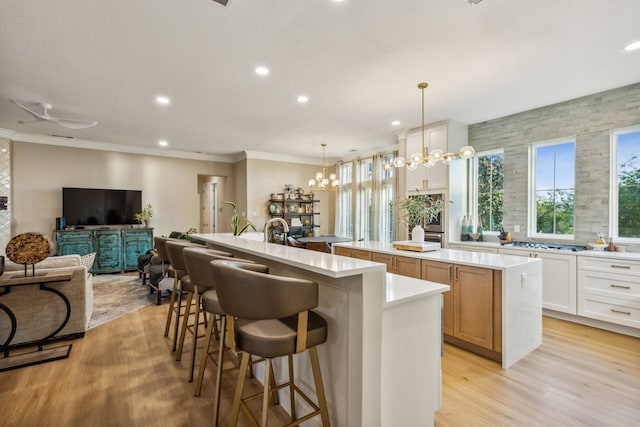 kitchen with a spacious island, pendant lighting, white cabinets, light hardwood / wood-style flooring, and a chandelier