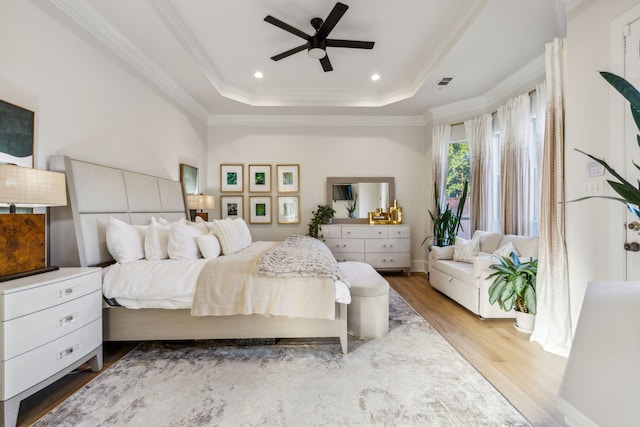 bedroom with ceiling fan, a raised ceiling, crown molding, and hardwood / wood-style floors