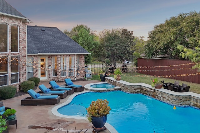 pool at dusk with an in ground hot tub and a patio