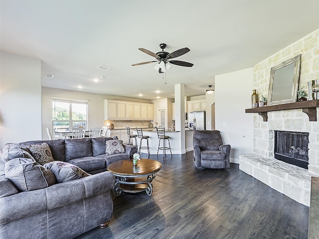 living room with a stone fireplace, dark hardwood / wood-style floors, and ceiling fan