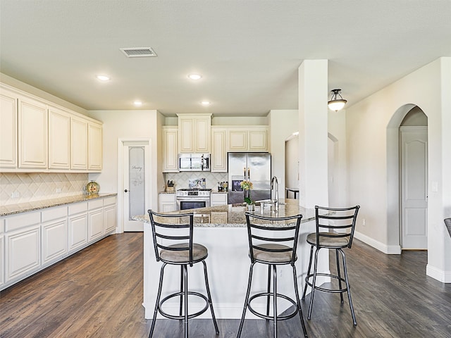 kitchen featuring appliances with stainless steel finishes, stone countertops, dark hardwood / wood-style floors, decorative backsplash, and a center island with sink