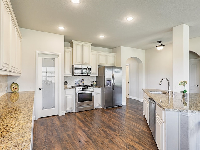 kitchen with decorative backsplash, dark wood-type flooring, sink, light stone countertops, and appliances with stainless steel finishes