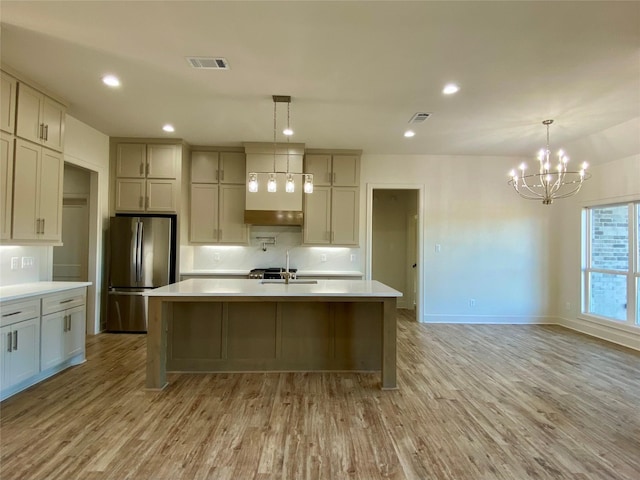 kitchen with a kitchen island with sink, decorative light fixtures, a notable chandelier, light hardwood / wood-style floors, and stainless steel refrigerator