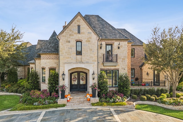 6408 Drawbridge Ln, Plano, TX 75024 - french country home featuring stone siding, french doors, a chimney, a high end roof, and a balcony
