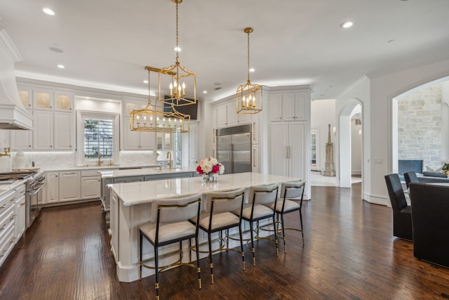 kitchen with a kitchen bar, a center island, stainless steel built in refrigerator, hanging light fixtures, and dark hardwood / wood-style floors