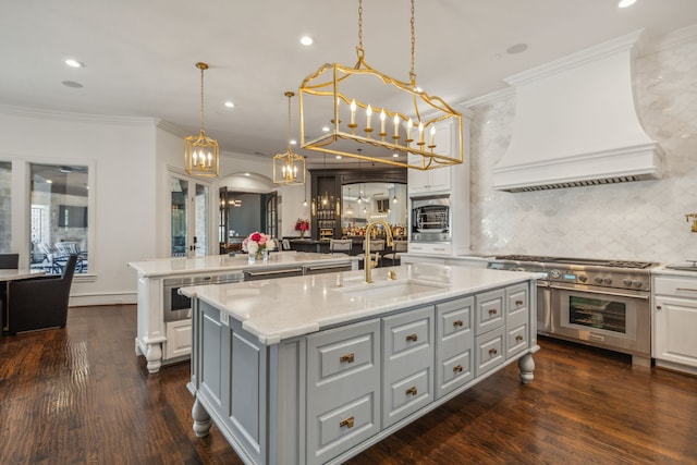 kitchen with a kitchen island with sink, stainless steel appliances, sink, pendant lighting, and dark hardwood / wood-style flooring