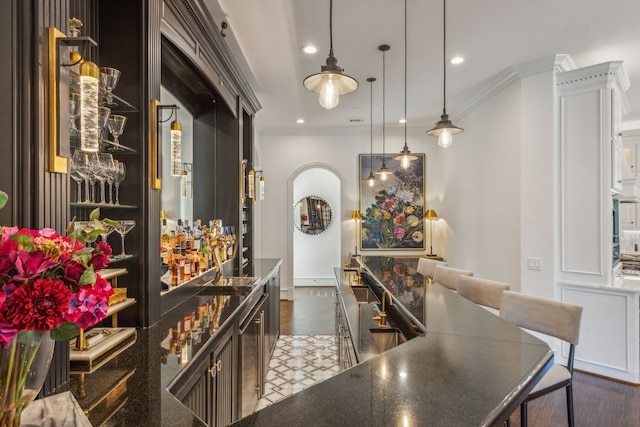 bar featuring crown molding, dark brown cabinetry, dark hardwood / wood-style floors, and hanging light fixtures