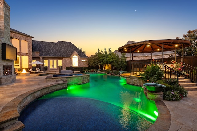 pool at dusk with a gazebo, a patio area, and an in ground hot tub