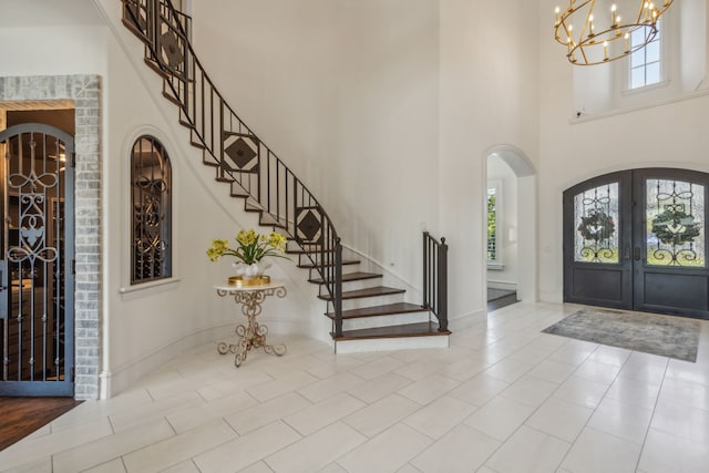 tiled entrance foyer with french doors, a chandelier, and a high ceiling