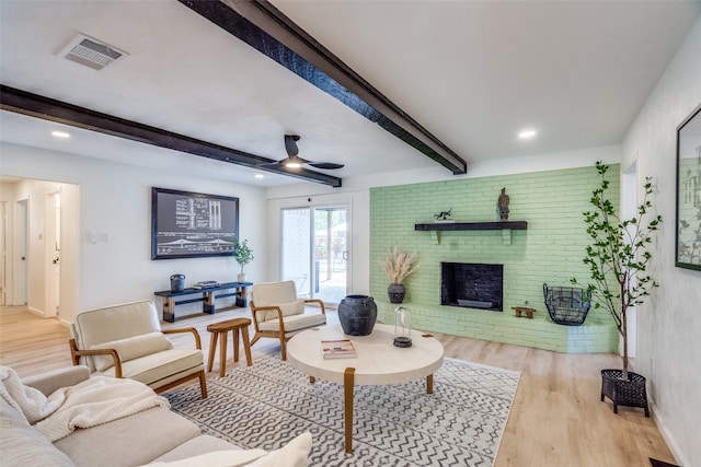 living room featuring a fireplace, beam ceiling, light wood-type flooring, and ceiling fan