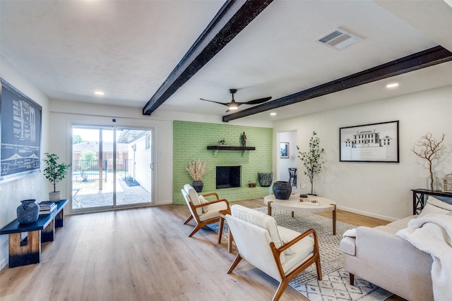 living room with light hardwood / wood-style floors, beamed ceiling, a brick fireplace, and ceiling fan