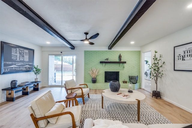 living room featuring washer / clothes dryer, ceiling fan, a brick fireplace, beamed ceiling, and light hardwood / wood-style floors