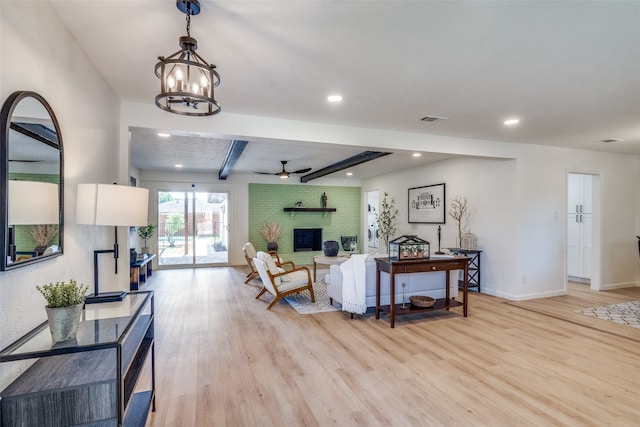 living room featuring ceiling fan with notable chandelier, light hardwood / wood-style floors, beam ceiling, and a fireplace