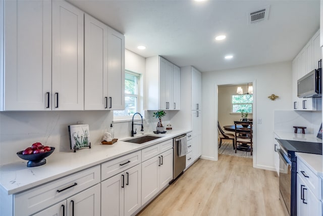 kitchen with appliances with stainless steel finishes, white cabinets, sink, and light wood-type flooring