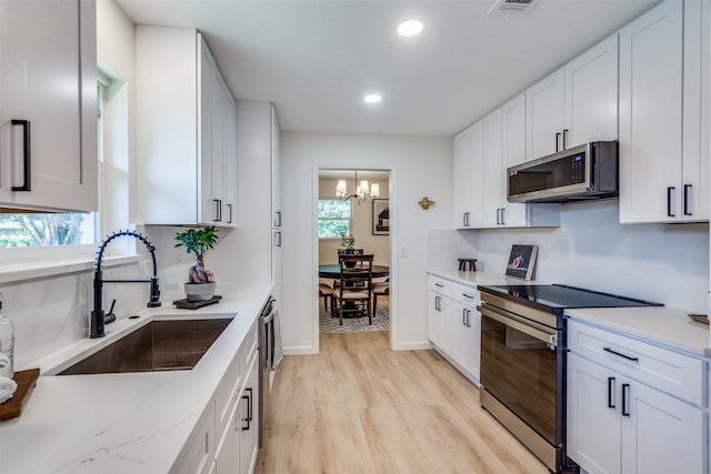 kitchen with white cabinets, an inviting chandelier, light wood-type flooring, sink, and stainless steel appliances