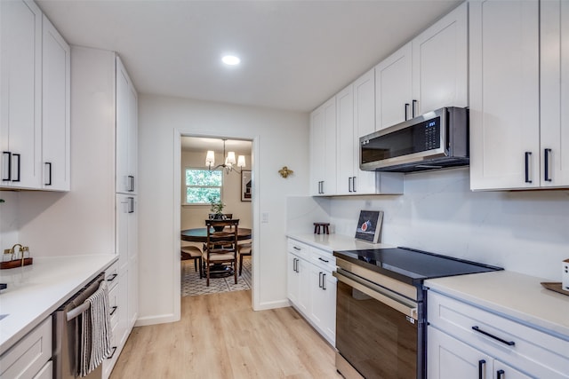 kitchen with white cabinets, a notable chandelier, stainless steel appliances, and light wood-type flooring