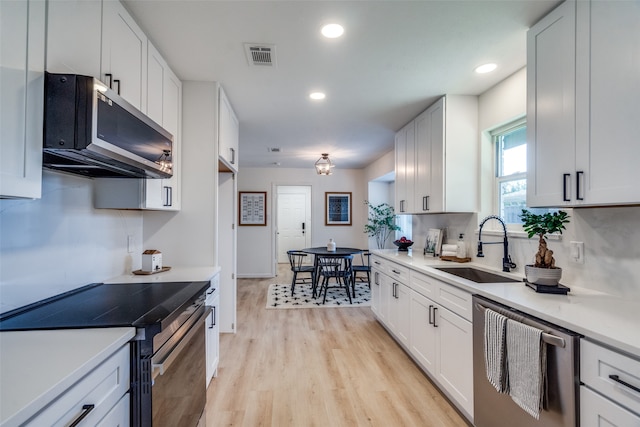 kitchen featuring appliances with stainless steel finishes, sink, white cabinetry, decorative backsplash, and light hardwood / wood-style flooring