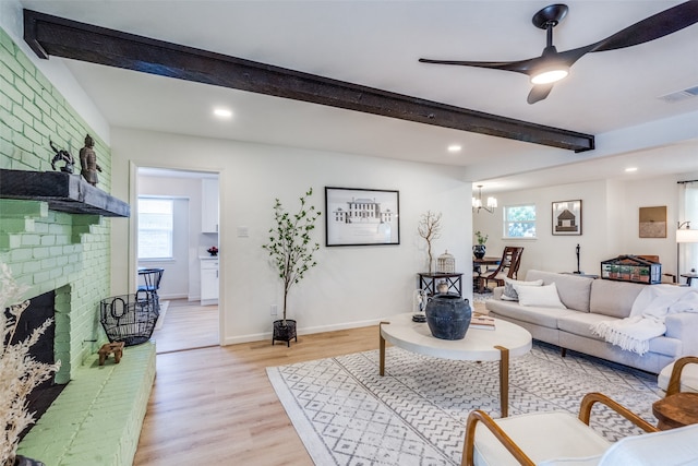 living room with light hardwood / wood-style floors, a fireplace, beamed ceiling, and ceiling fan with notable chandelier