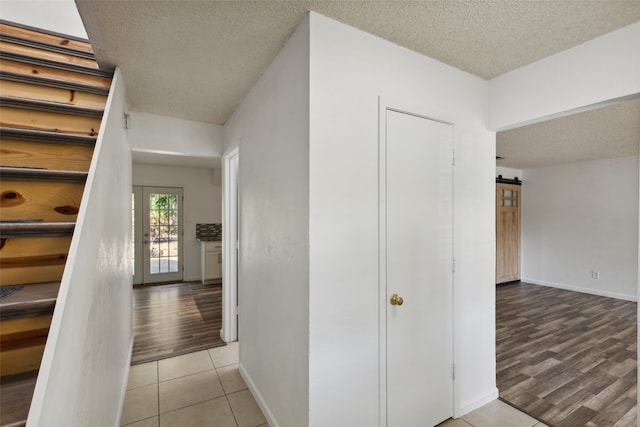 hallway featuring a barn door, light hardwood / wood-style floors, a textured ceiling, and french doors