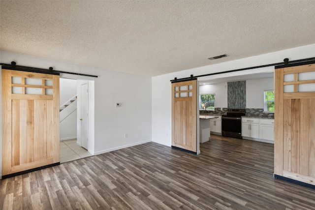 unfurnished living room featuring a barn door, dark hardwood / wood-style floors, and a textured ceiling