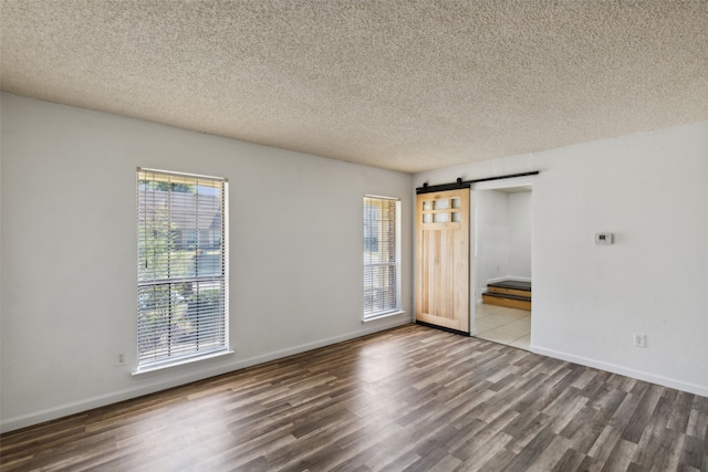 unfurnished room with a textured ceiling, a barn door, and dark hardwood / wood-style floors